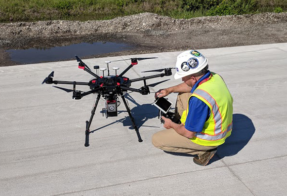 drone pilot with controller kneeling next to a RIEGL miniVUX 2UAV UAV-LiDAR system